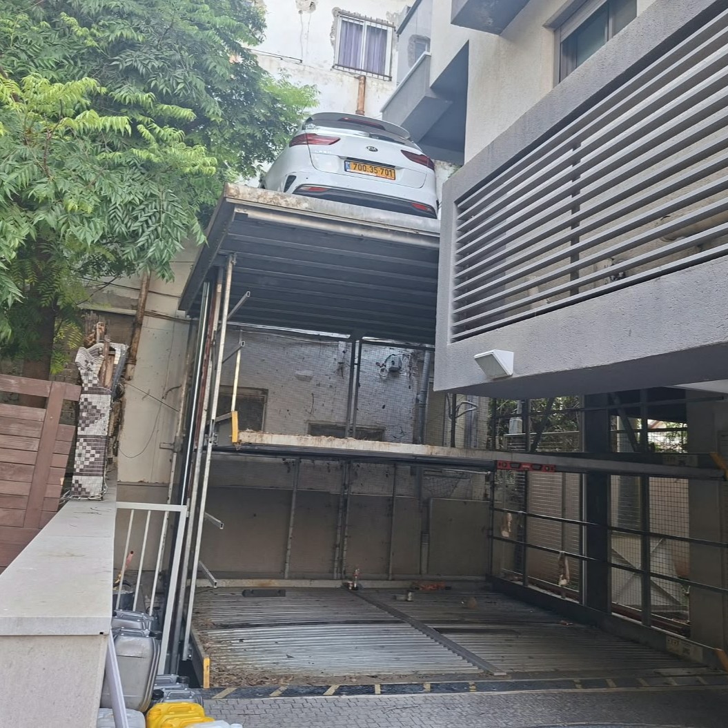 רכב לבן במפלס העליון של מתקן חניה לצד בניין